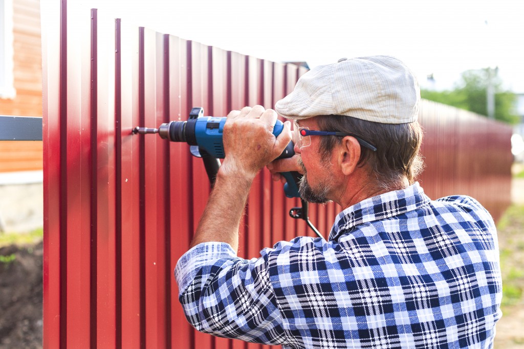 man with a drill builds metal fence