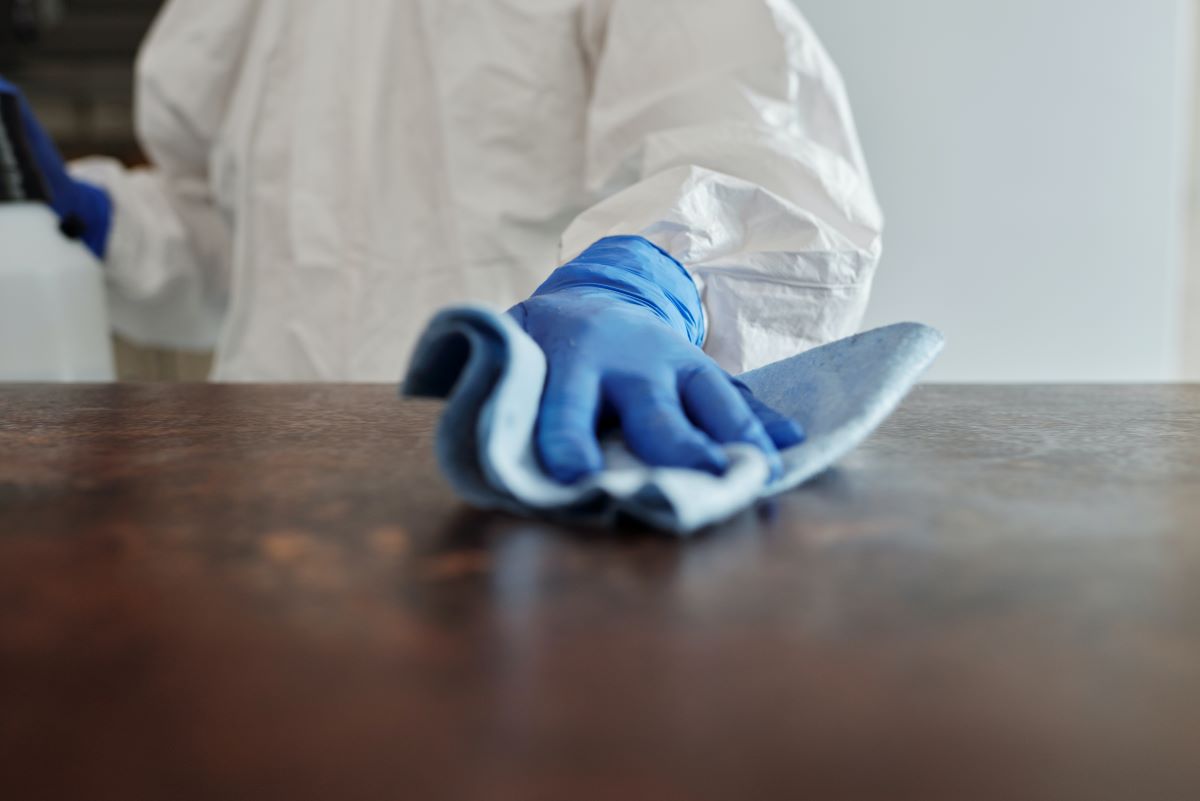 wiping wooden table in full PPE