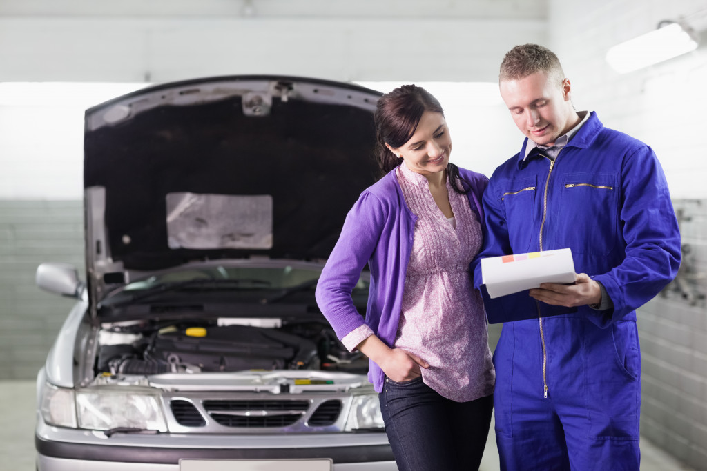 a woman standing beside a mechanic showing a document with car on the background