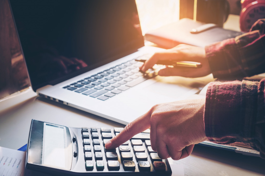 A person using a calculator and laptop to manage their finances