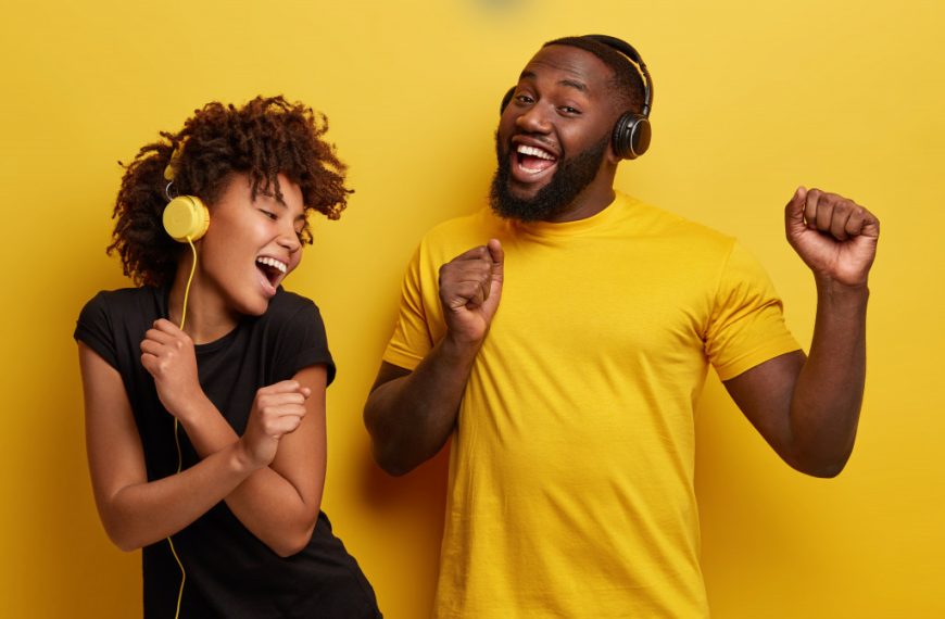 A man and a woman wearing headphones and dancing happily while listening